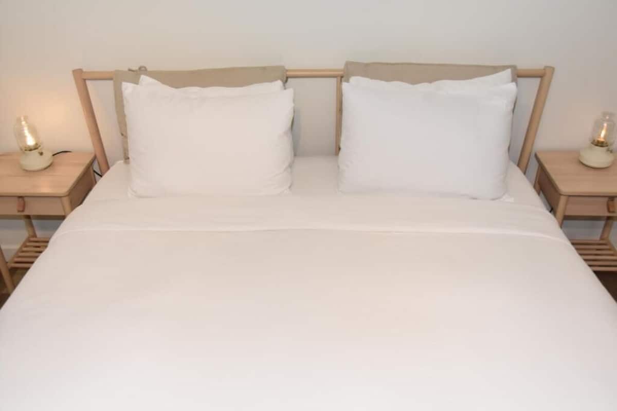 A bed with white bedding, two pillows, and a wooden headboard. There are two bedside tables with lamps on either side of the bed.