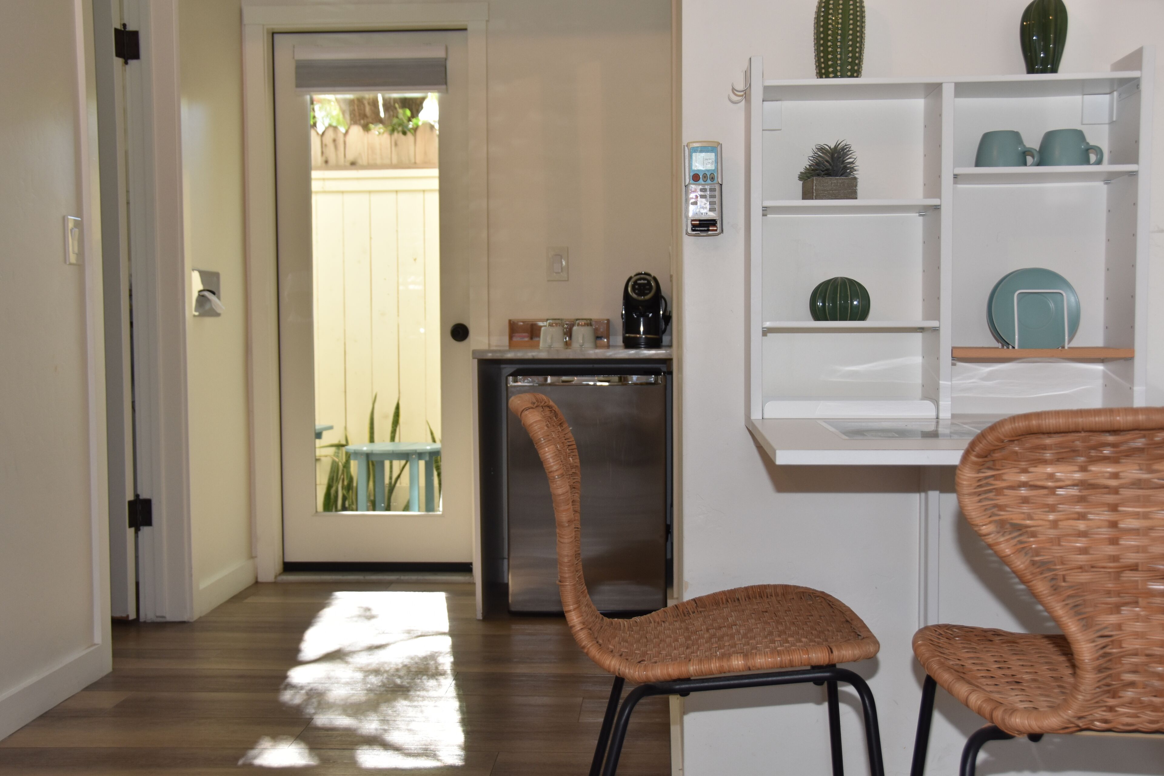 A kitchen area with a refrigerator, a coffee maker, and wicker chairs.