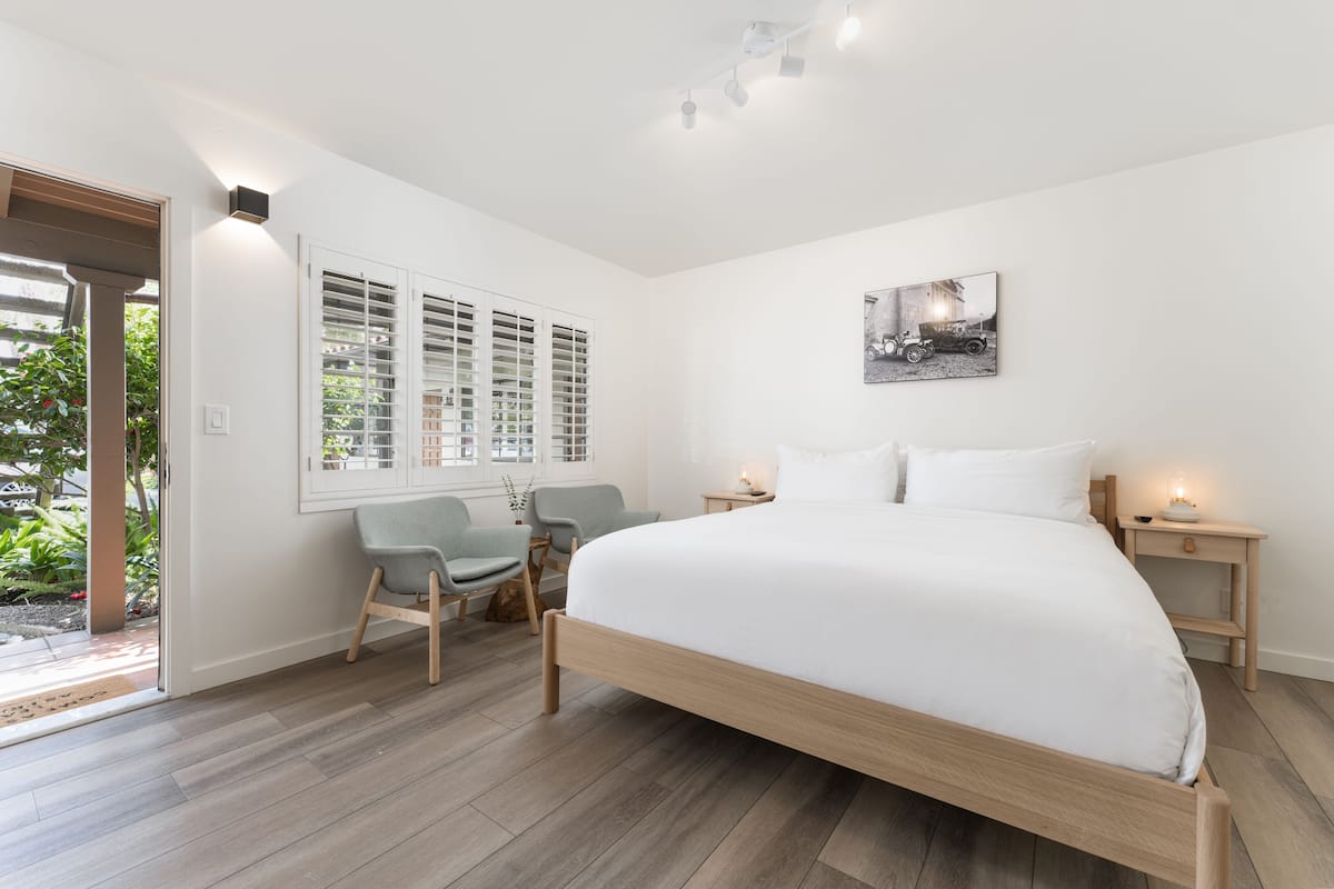 A bedroom with a large bed, two bedside tables, a chair, and a window with blinds.