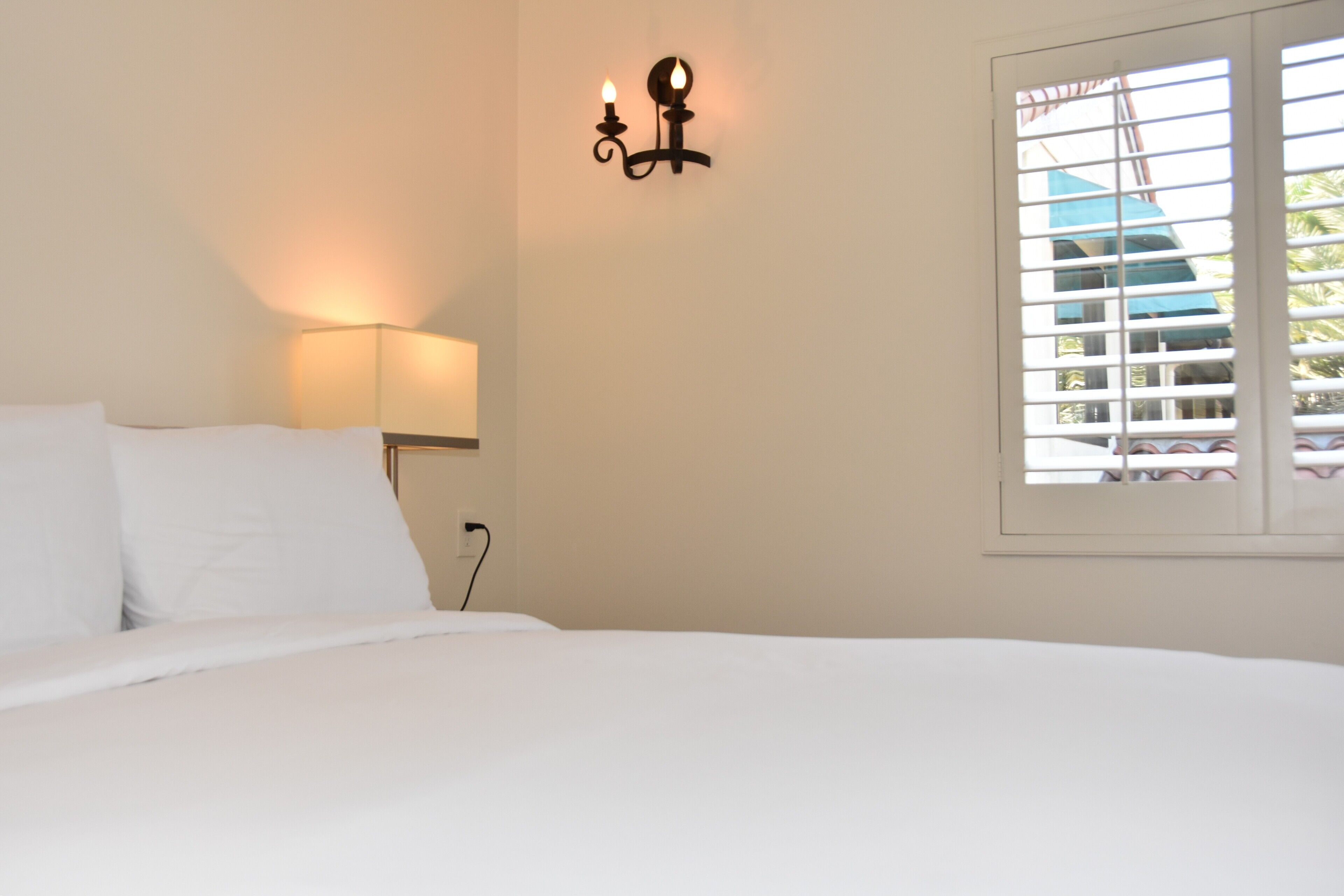 Een slaapkamer met een bed, een wandlamp en een raam met jaloezieën.