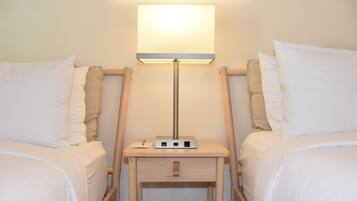 Une chambre d’hôtel avec deux lits, une table de chevet avec une lampe et une prise électrique.