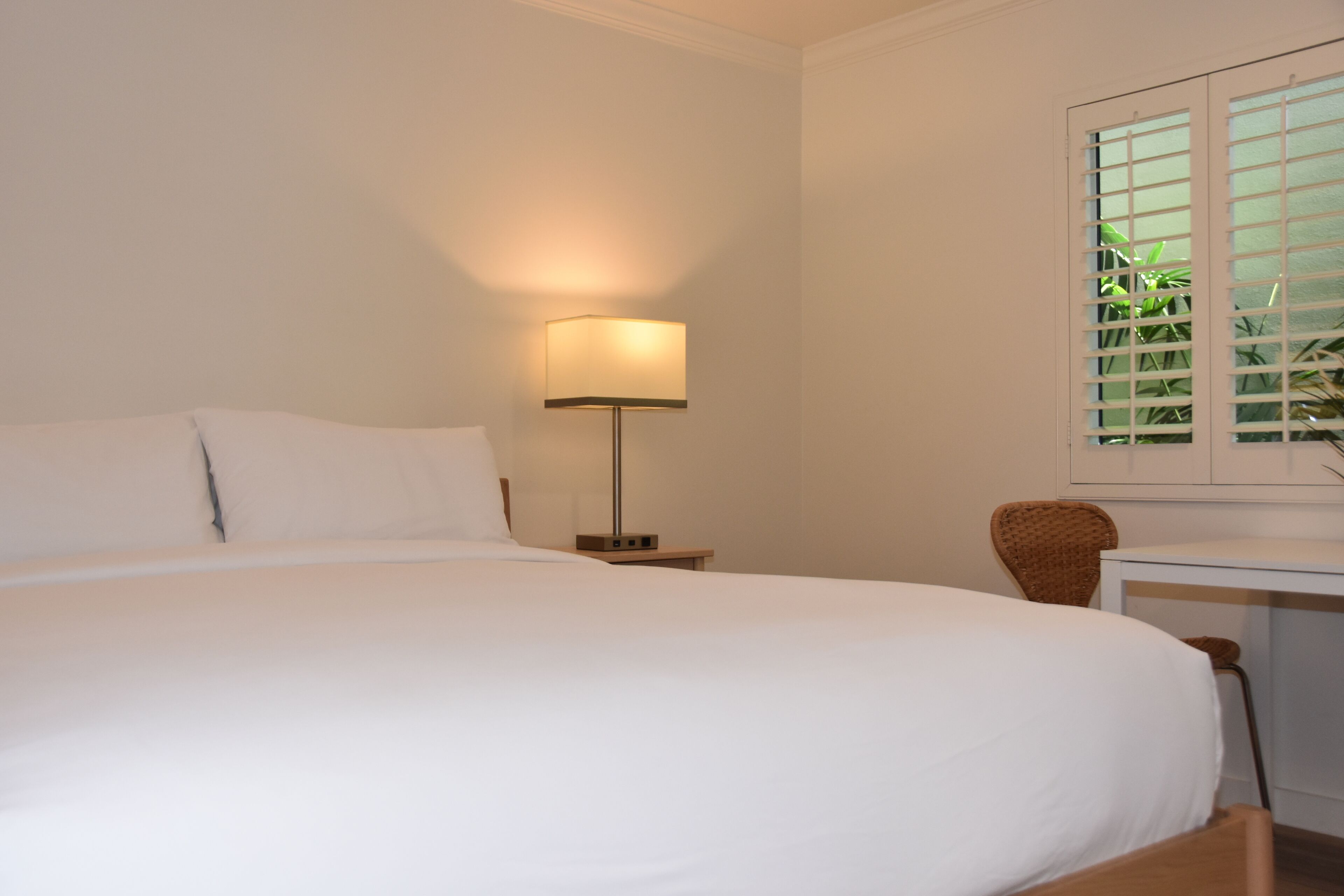 A hotel room with a large bed, a bedside table with a lamp, a chair, and a window with blinds.