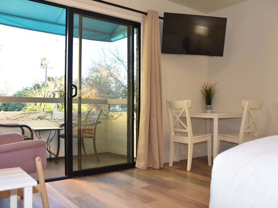 Quarto de hotel com porta de correr de vidro que dá para um pátio externo, uma TV de tela plana fixada na parede e uma pequena mesa com cadeiras.