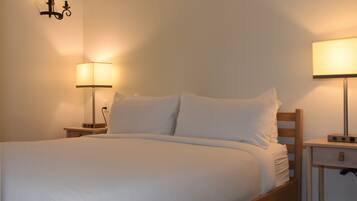 A neatly made bed with white linens, two bedside lamps, and a small wooden nightstand with a lamp.