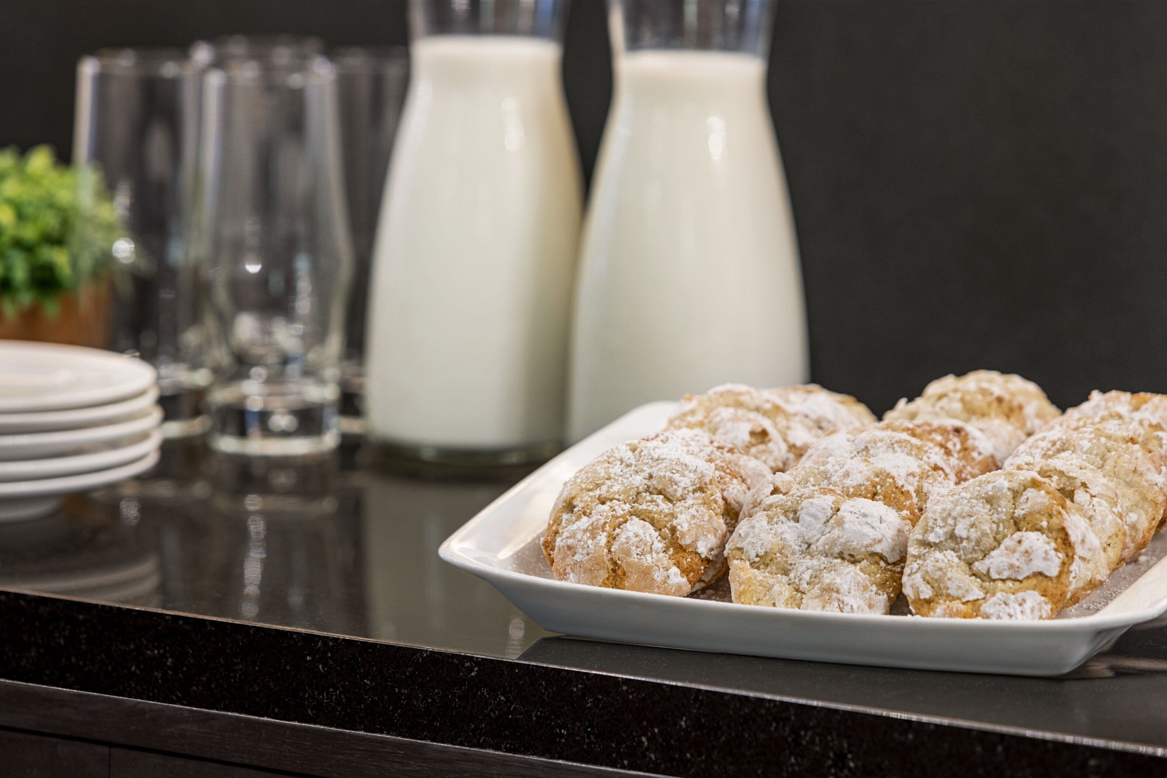 Une assiette de pâtisseries saupoudrées de sucre glace, un verre de lait et une bouteille de lait posés sur un comptoir.