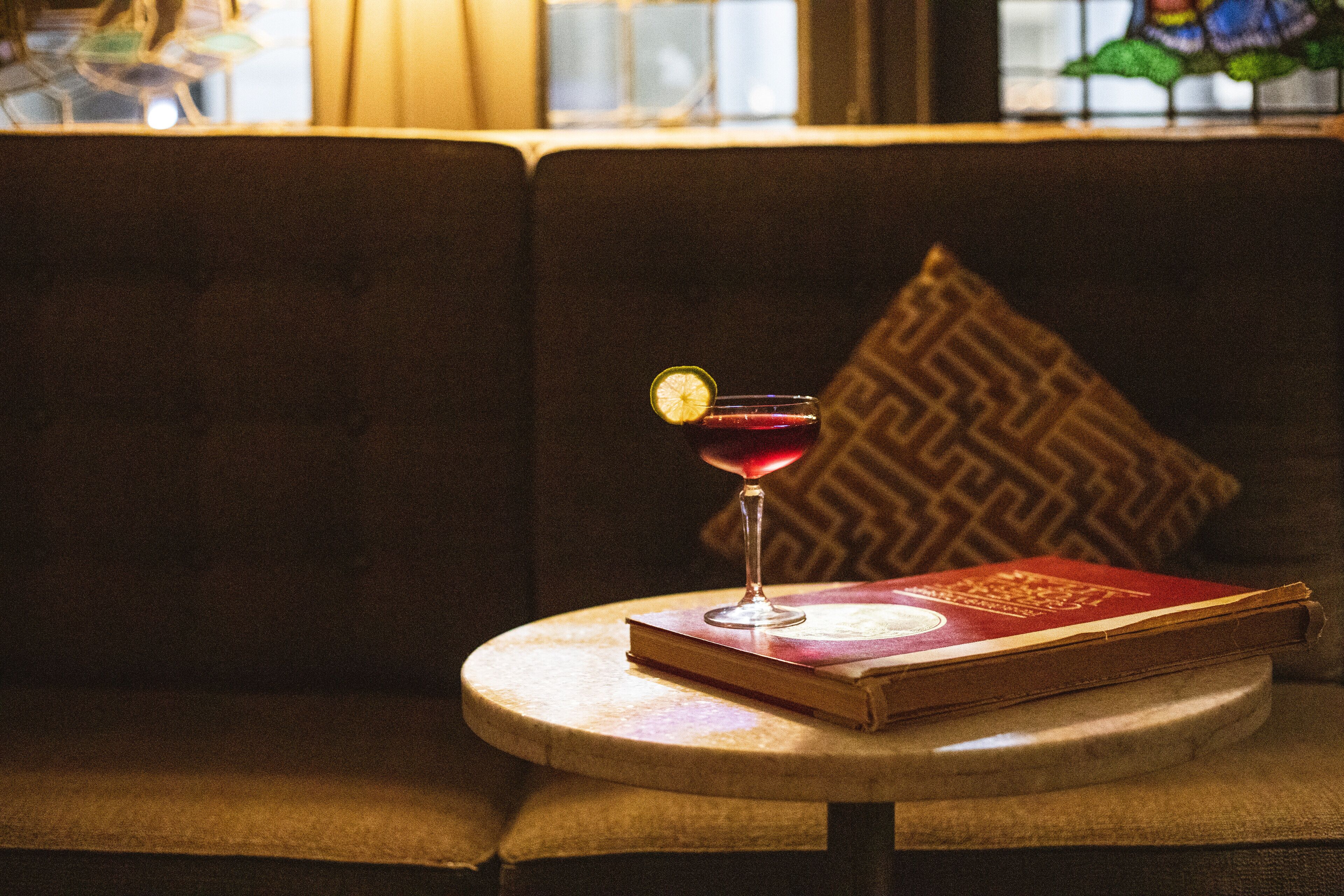 A round table with a book and a glass of red drink with a lime garnish.
