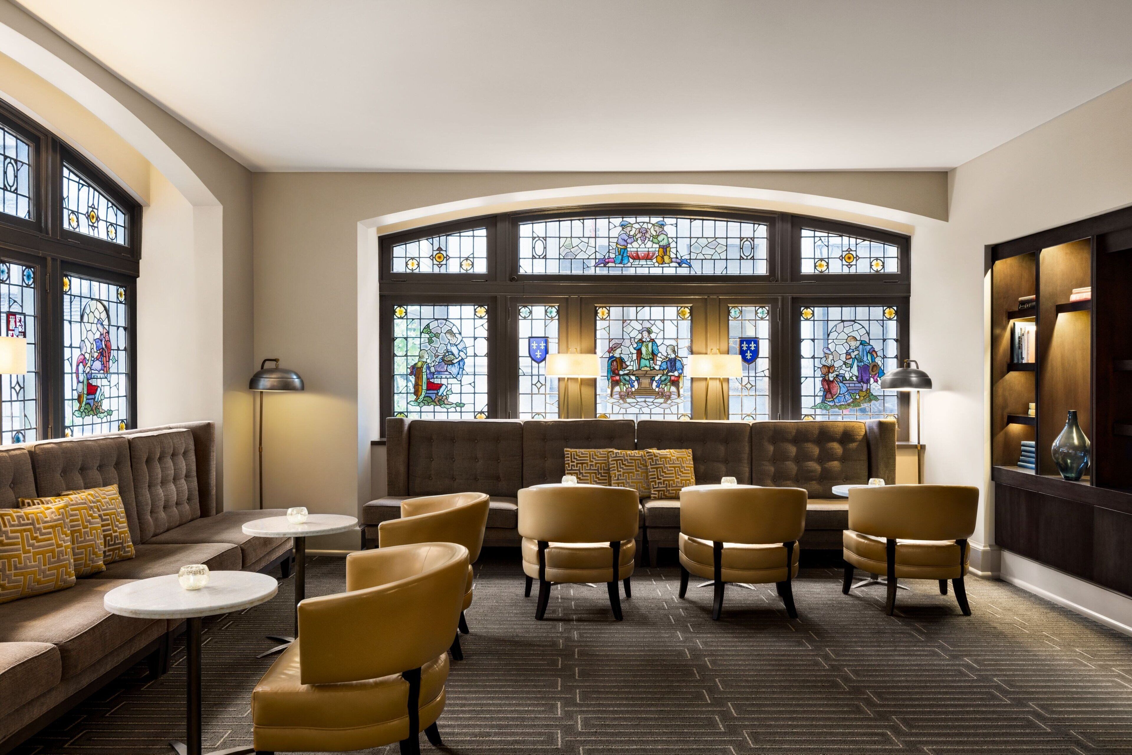 A hotel lobby with a sofa, armchairs, and a stained glass window.