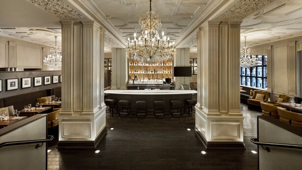 A bar area with a central bar, multiple stools, and a chandelier. - Magnolia Hotel St. Louis, a Tribute Portfolio Hotel (St. Louis)