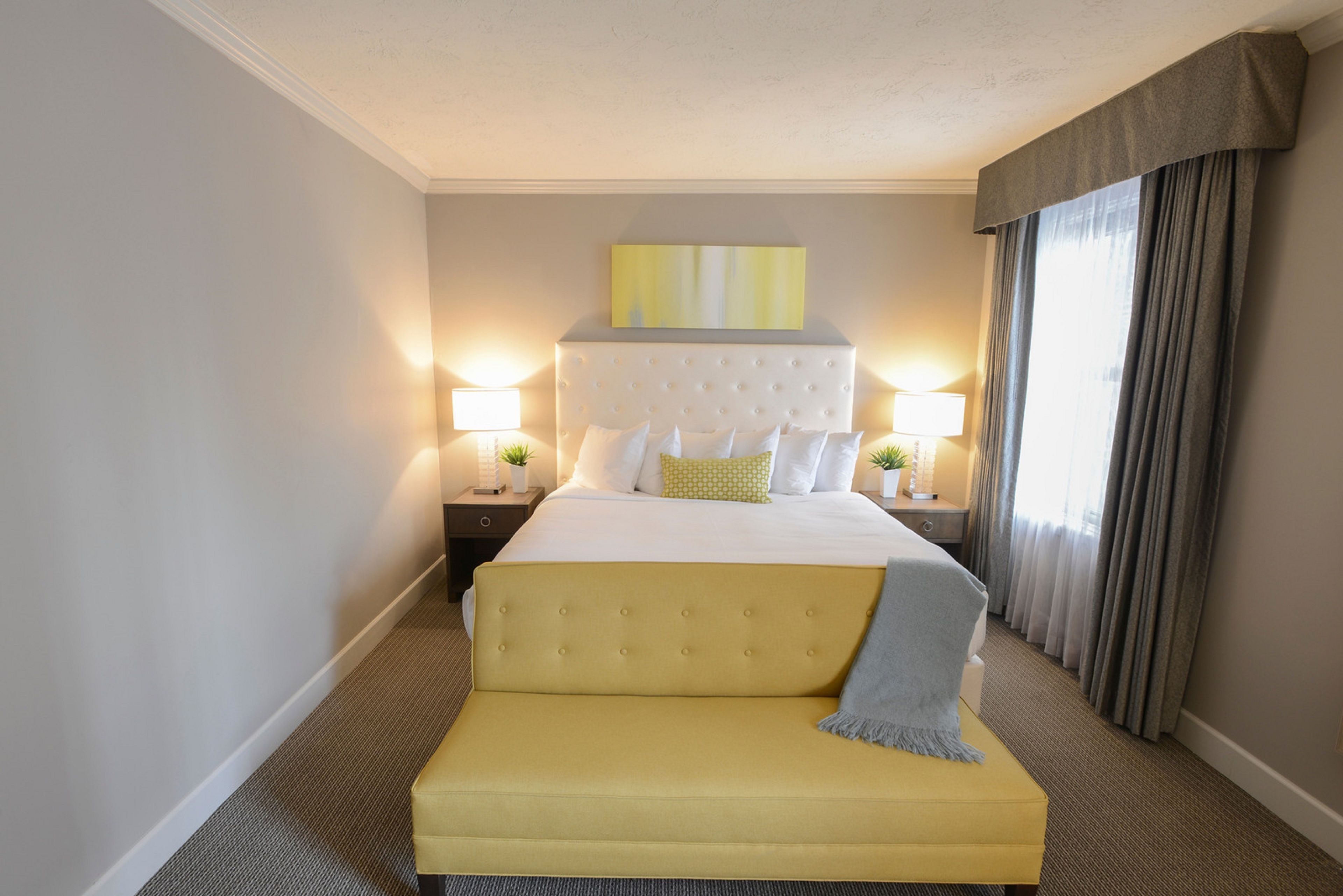 A hotel room with a large bed, two bedside tables with lamps, a bench, and a painting on the wall.