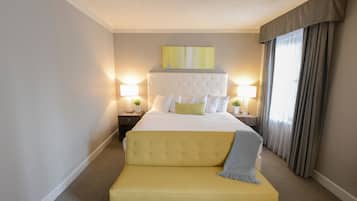 A hotel room with a large bed, two bedside tables with lamps, a bench, and a painting on the wall.