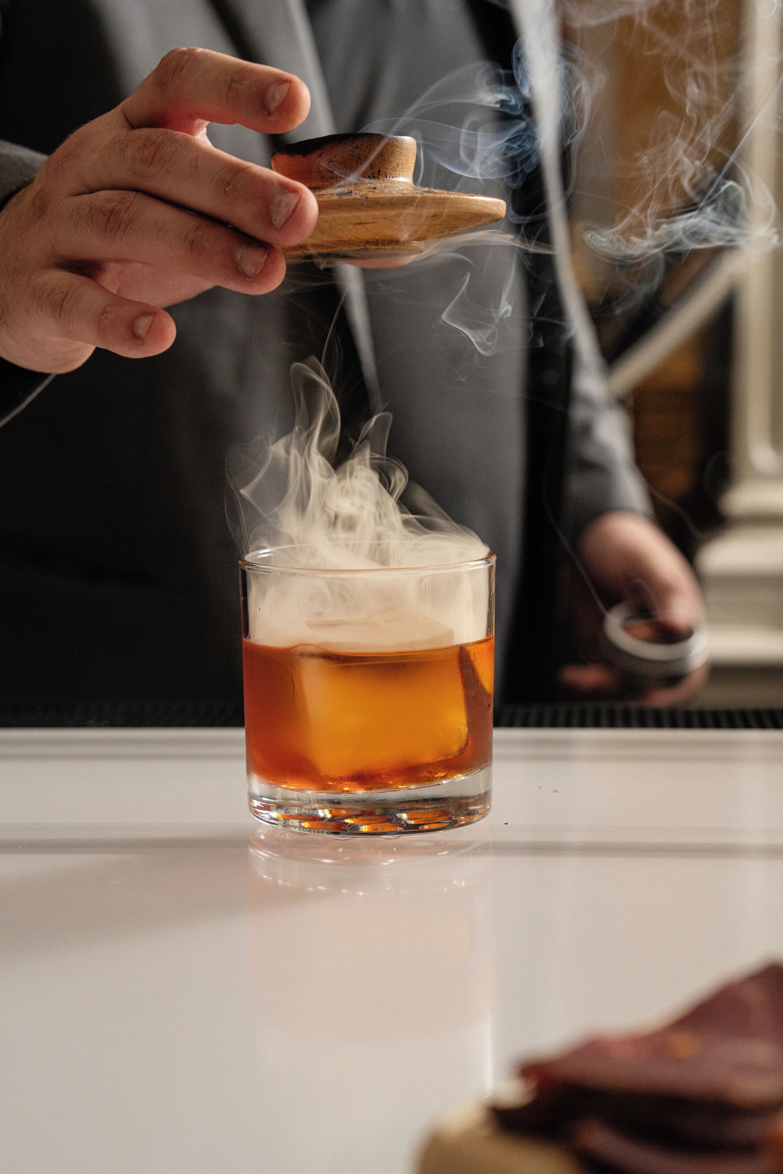 A person pouring a drink into a glass, with smoke rising from the glass.