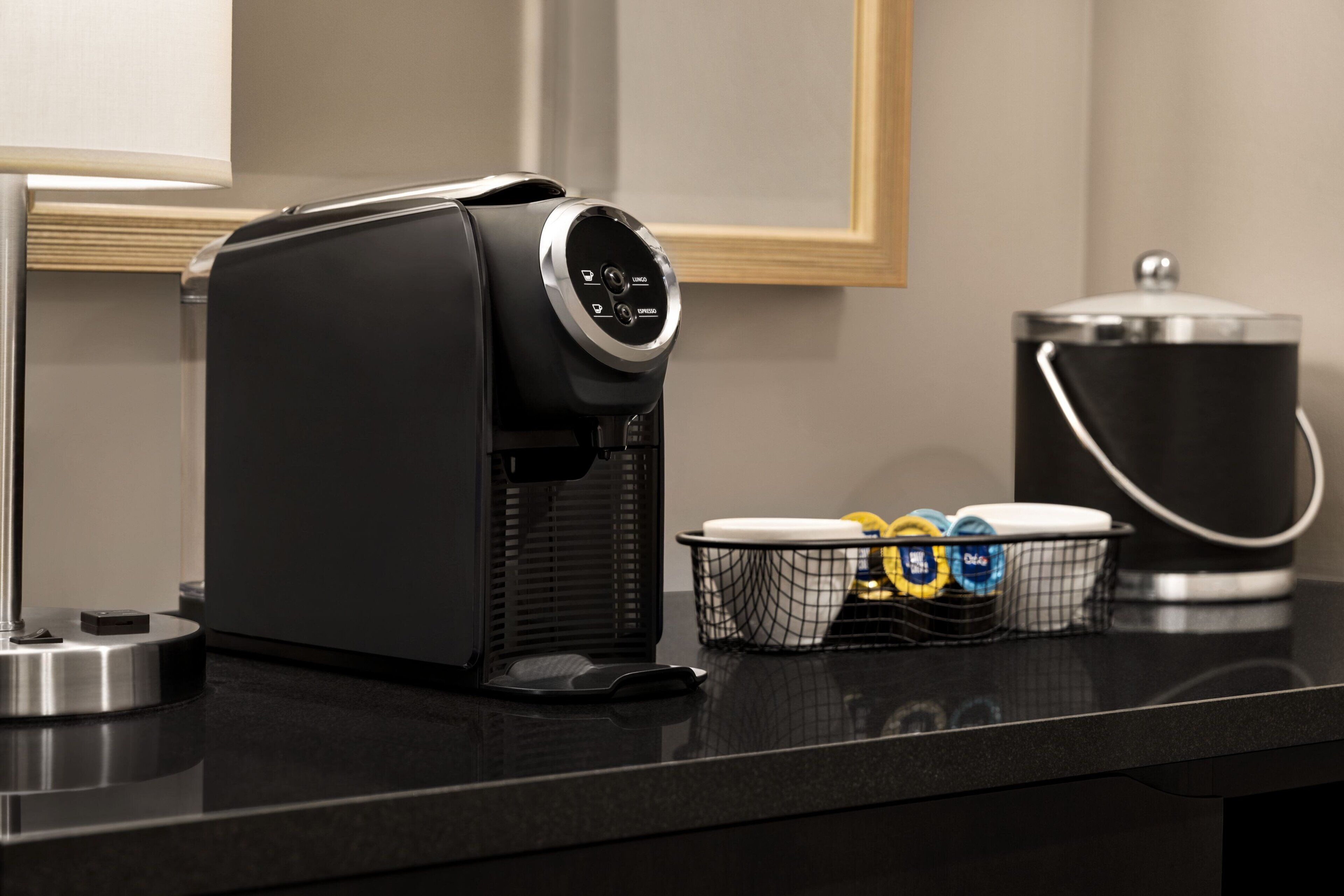 A coffee machine on a black countertop with a basket of disposable cups and a container of coffee pods.