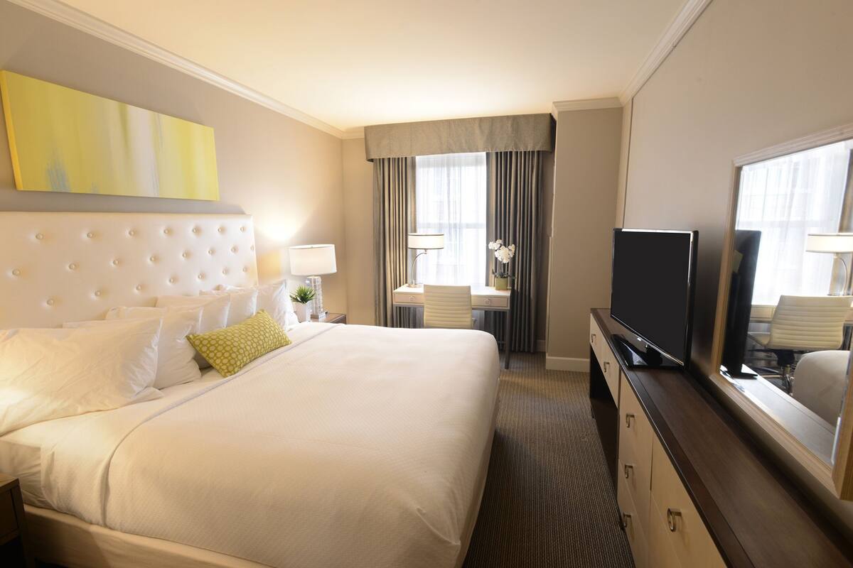 A hotel room with a large bed, a desk with a chair, a television, and a window with curtains.