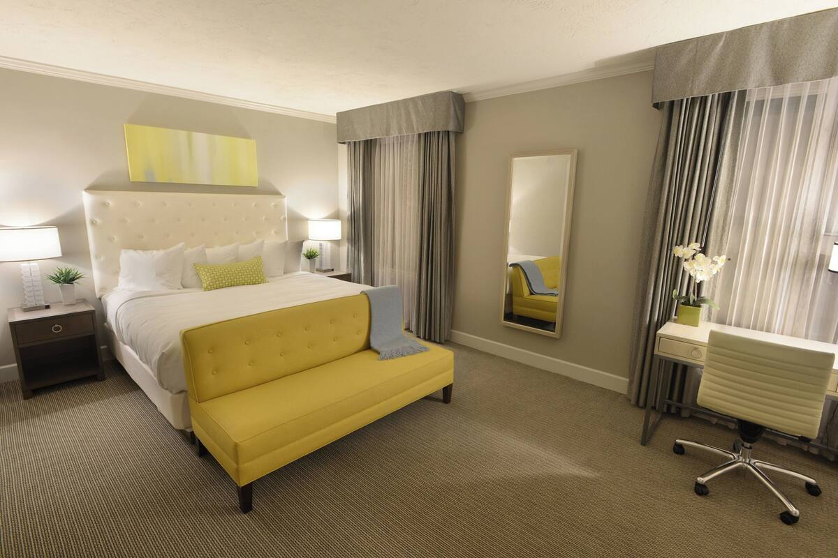 A hotel room with a large bed, a desk, a chair, and a mirror.