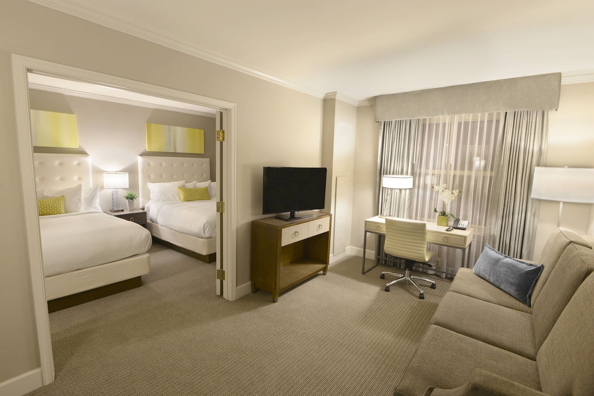 A hotel room with two beds, a desk, a TV, and a sofa.