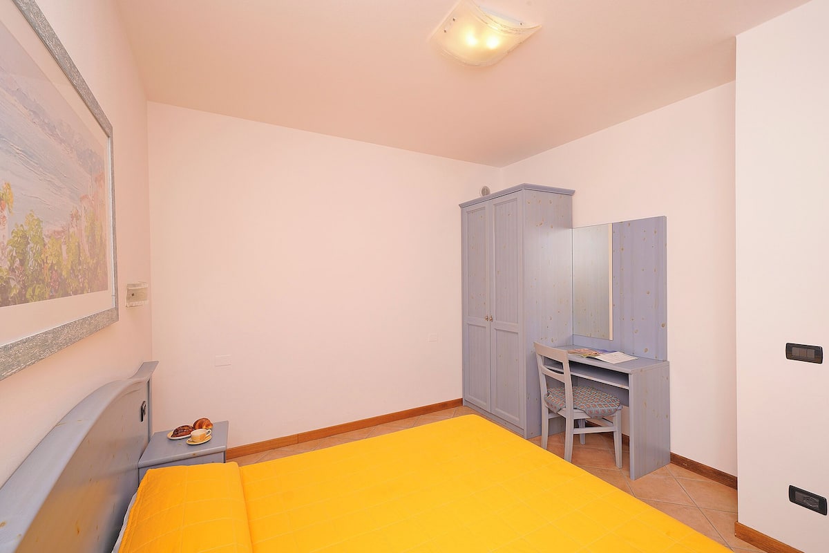 A bedroom with a bed, a desk, a wardrobe, and a painting on the wall.