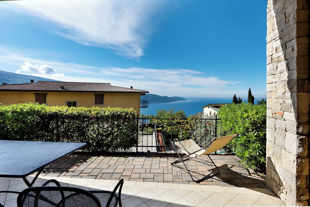 A patio with a table and chairs, a view of the sea, and a mountain in the background.