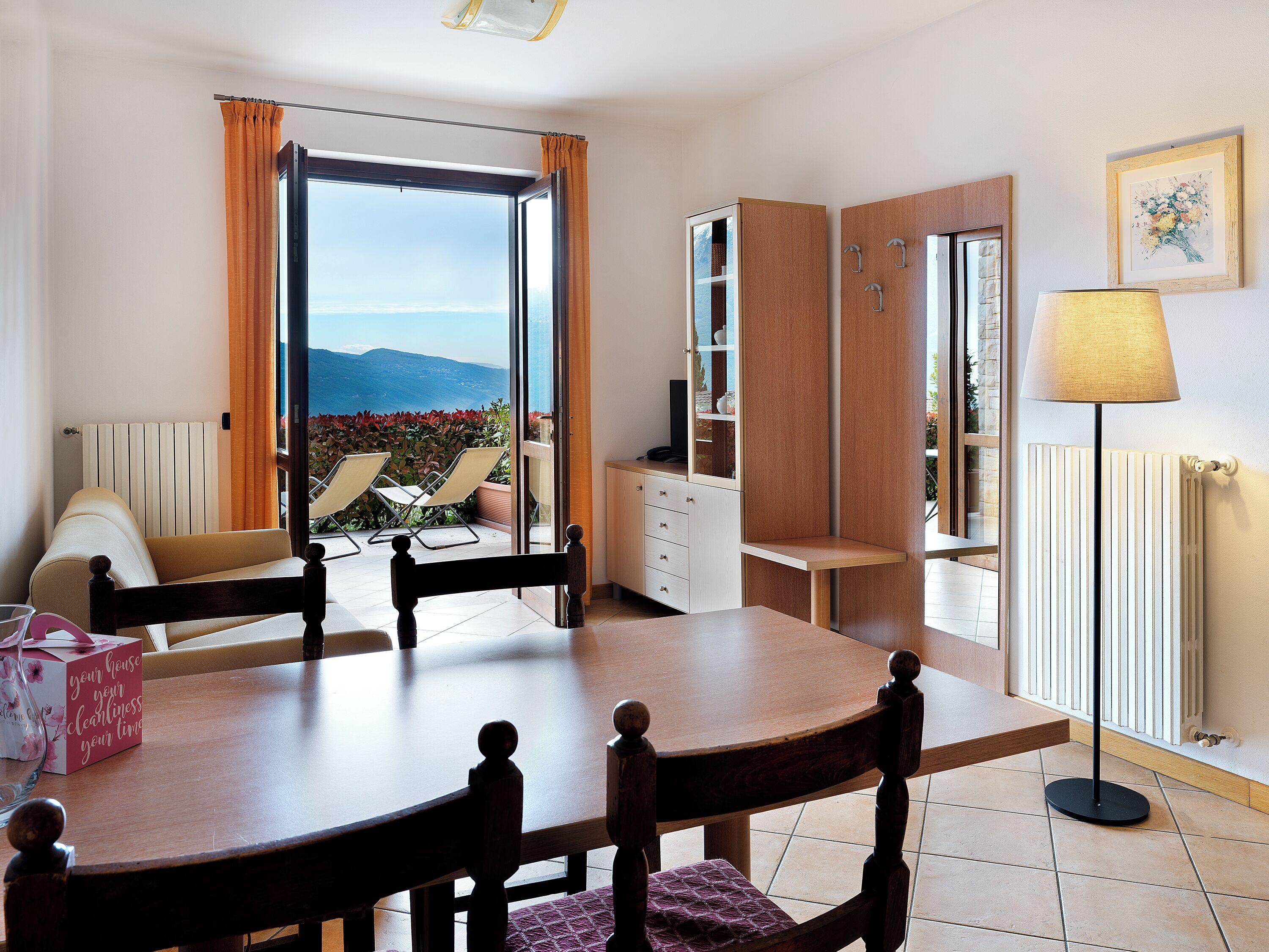 A dining area with a table, chairs, a sofa, a lamp, and a view of the outdoors.
