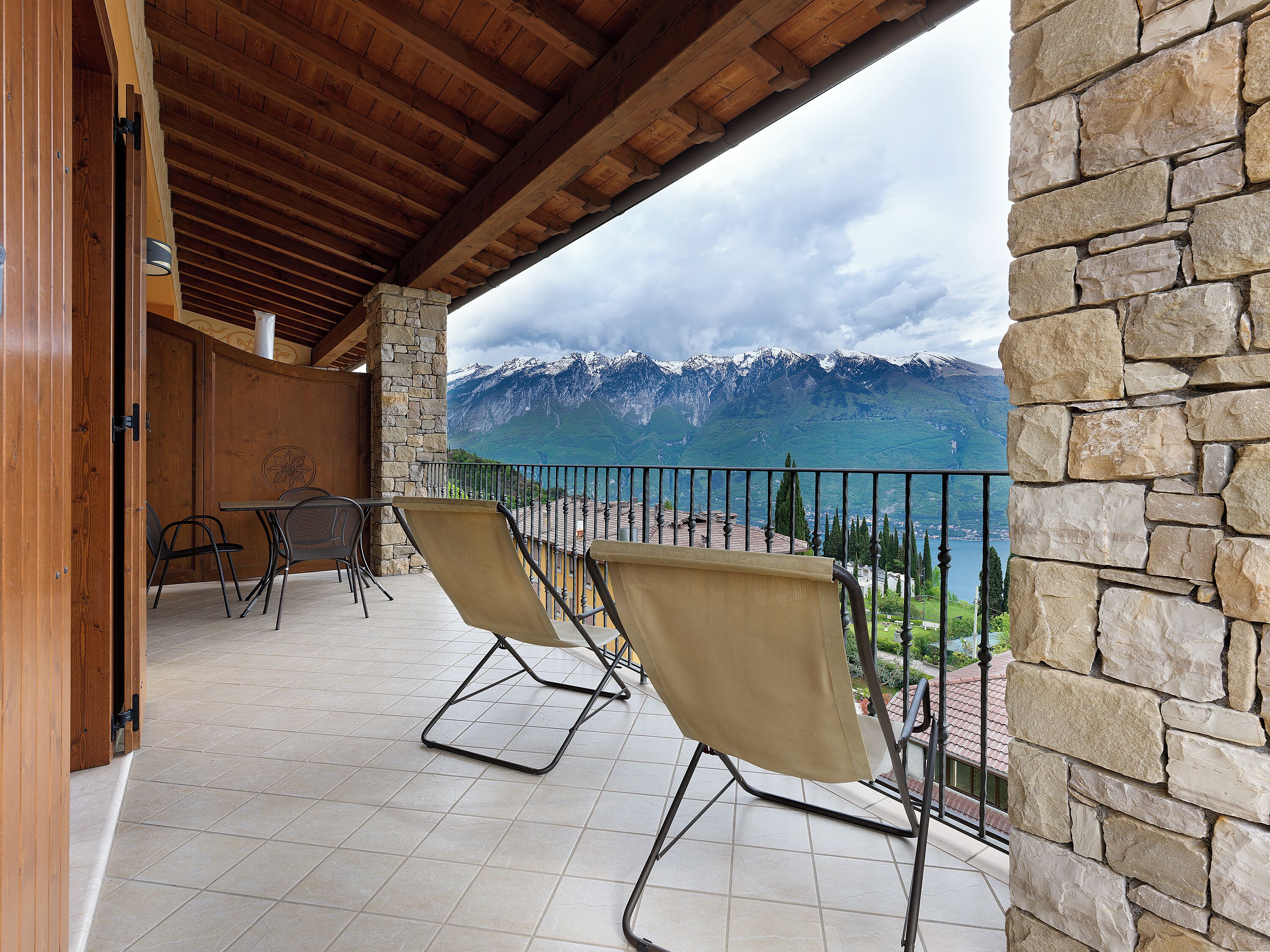 A balcony with a stone wall, a wooden ceiling, and a view of mountains.