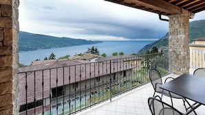 A balcony with a view of a lake and mountains, stone pillars, and a tiled floor. - Residence Besàss (Tignale)