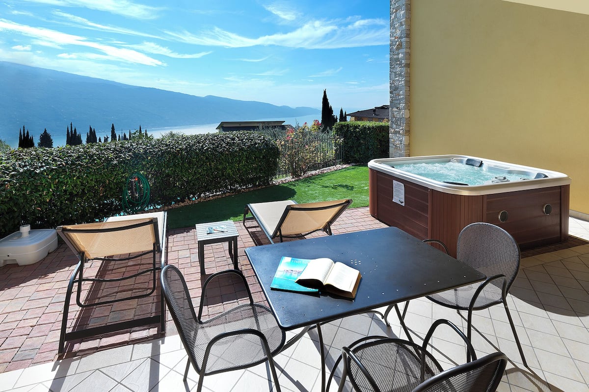 A patio with a hot tub, outdoor seating, and a view of the sea.