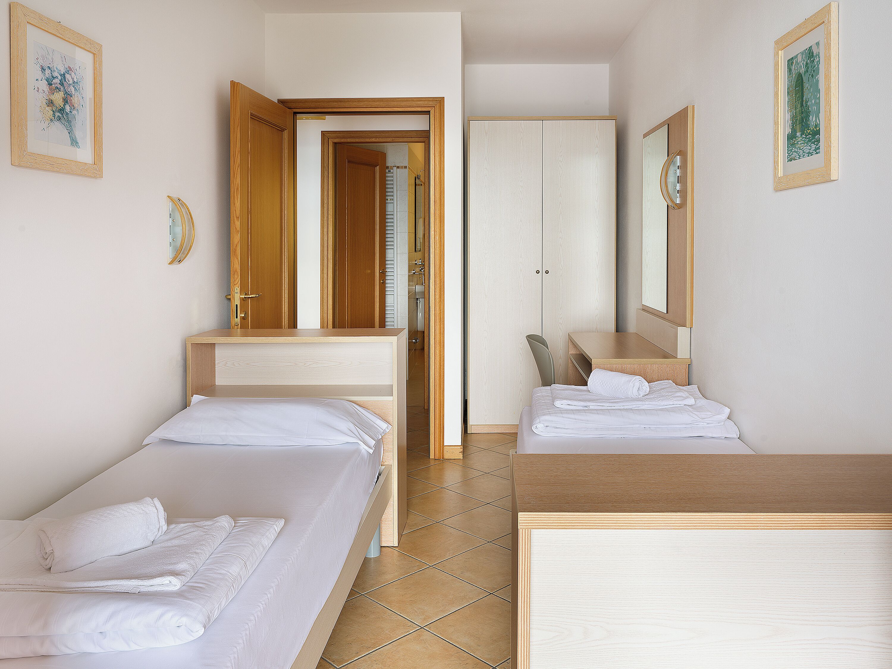 Ein Hotelzimmer mit zwei Betten, einem Schreibtisch, einem Spiegel und einem Kleiderschrank.