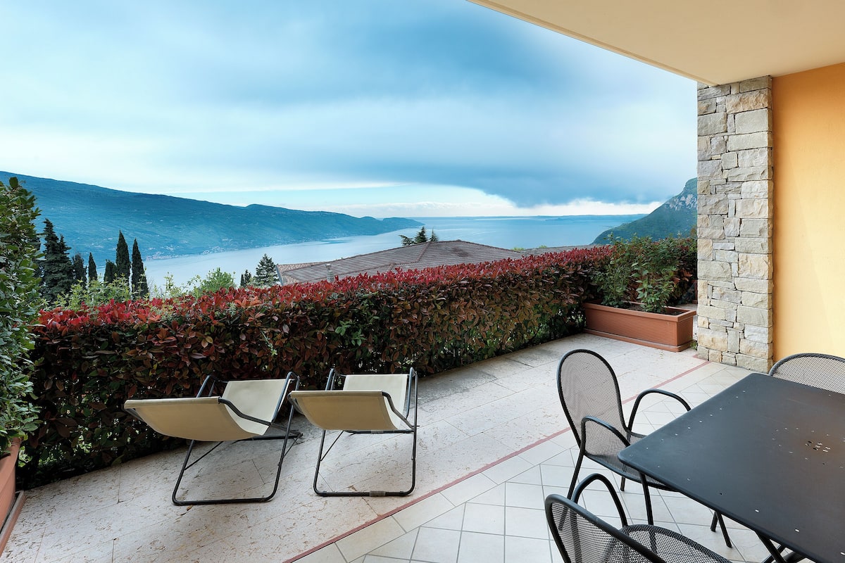 A terrace with a table and chairs, overlooking a lake and mountains.