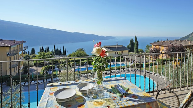 A terrace with a dining table set for four, overlooking a swimming pool and a mountainous landscape. - Residence Besàss (Tignale)