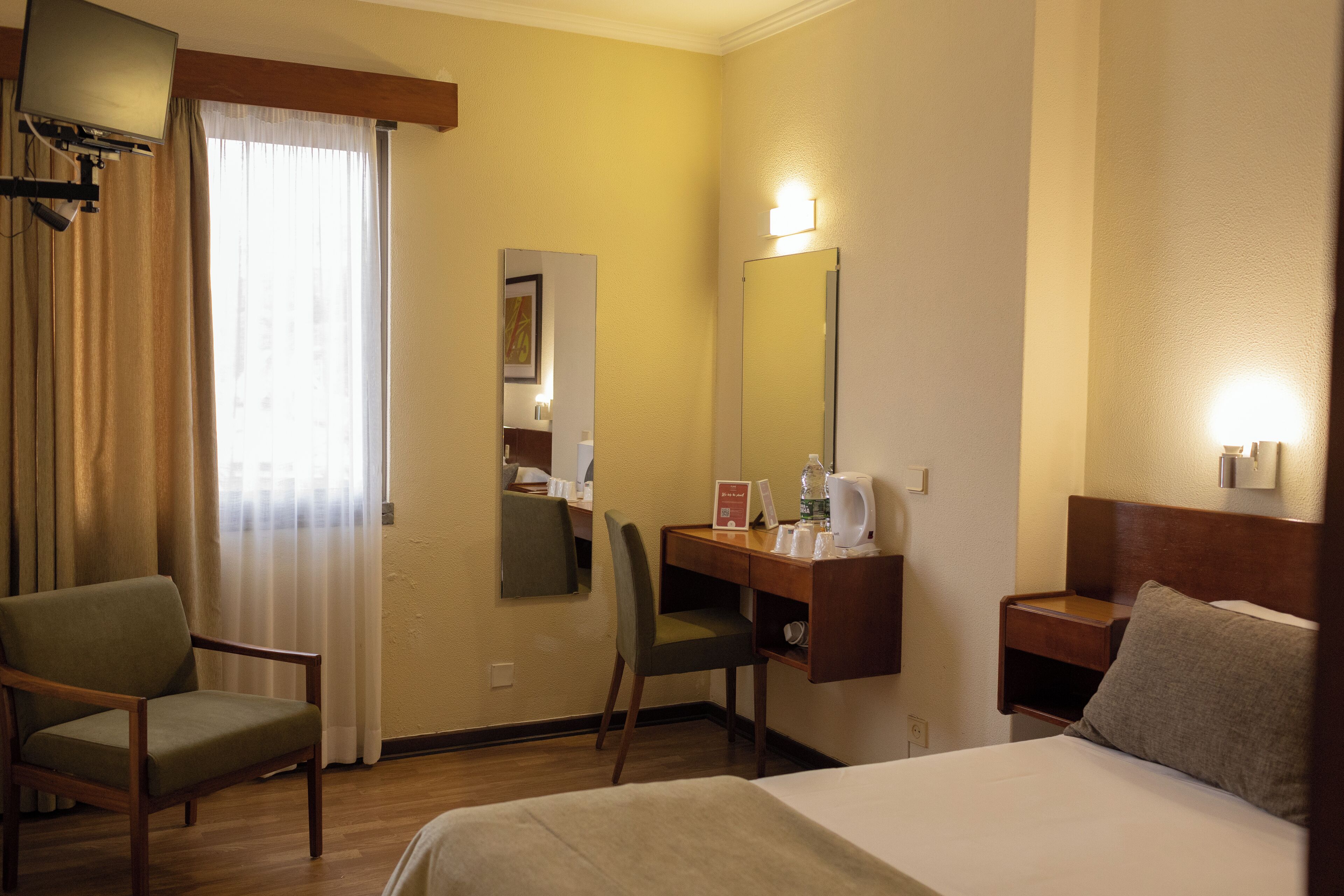 A hotel room with a bed, a desk with a chair, a television, and a mirror.