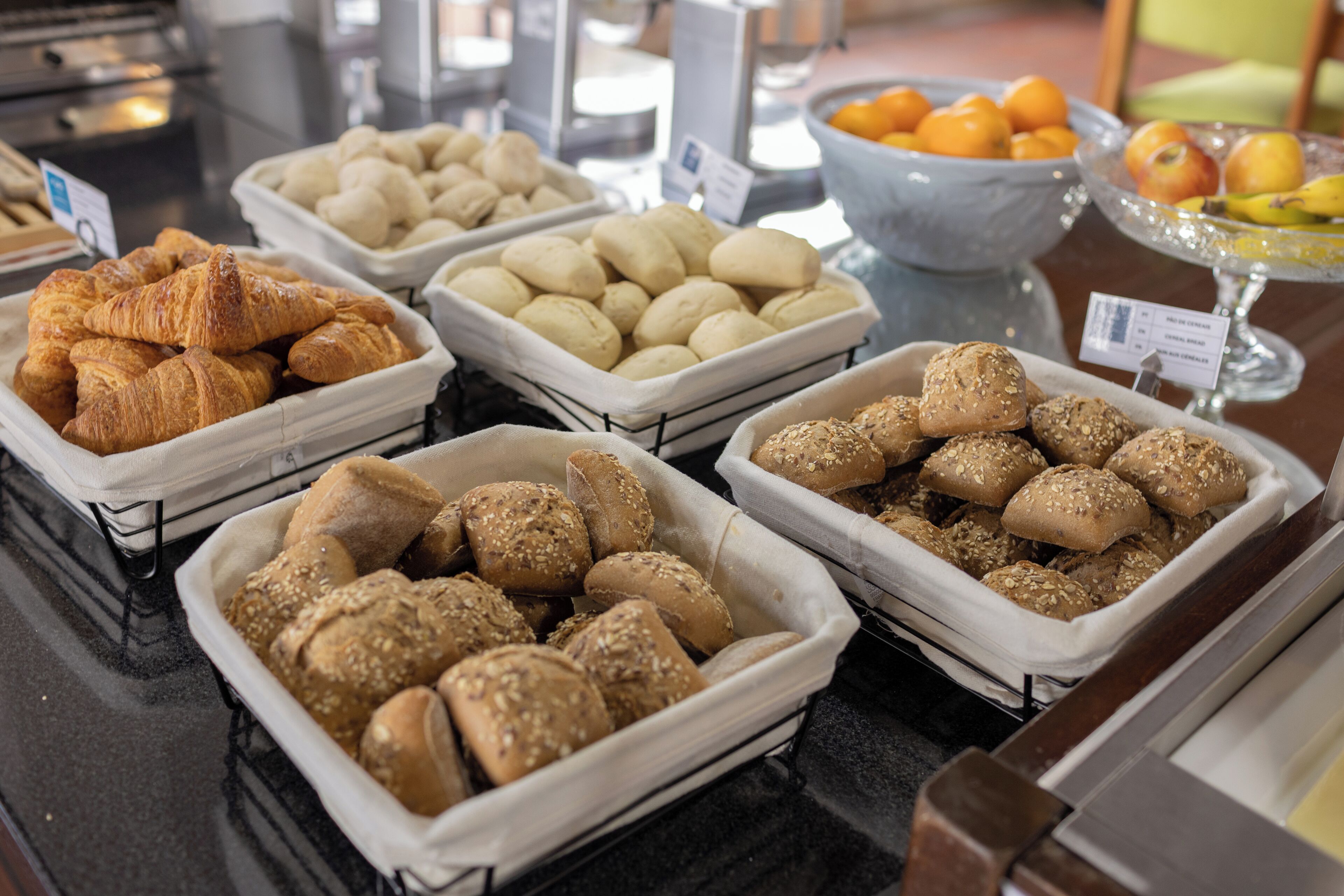 A buffet with various baked goods including croissants, bread rolls, and seeded buns.