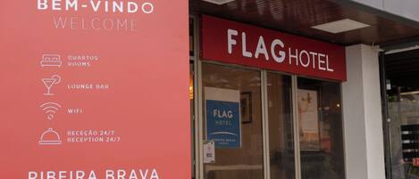 A hotel entrance with a large red sign displaying amenities such as rooms, lounge bar, WiFi, and 24/7 reception.