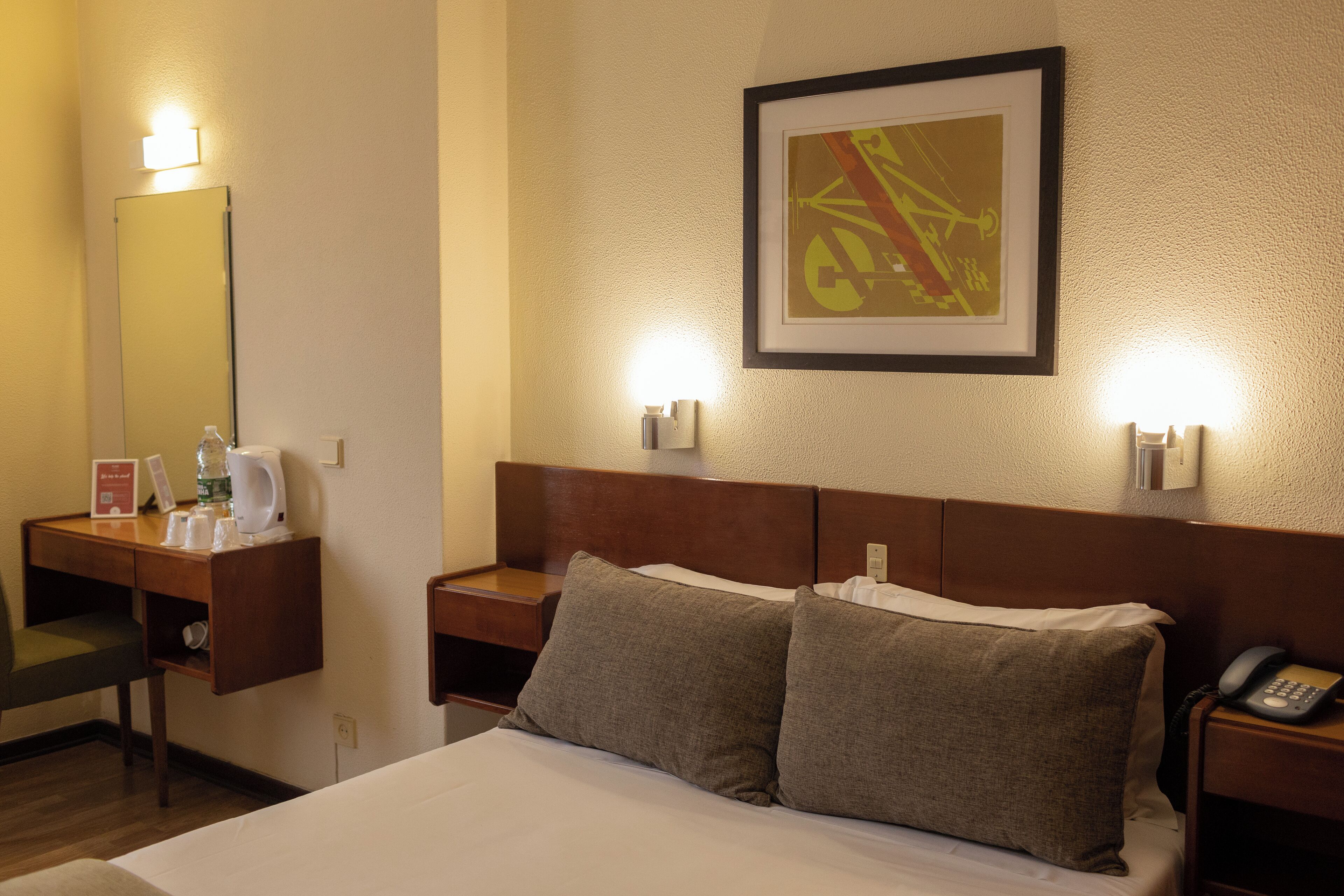 A hotel room with a bed, bedside table, lamp, and a framed picture on the wall.