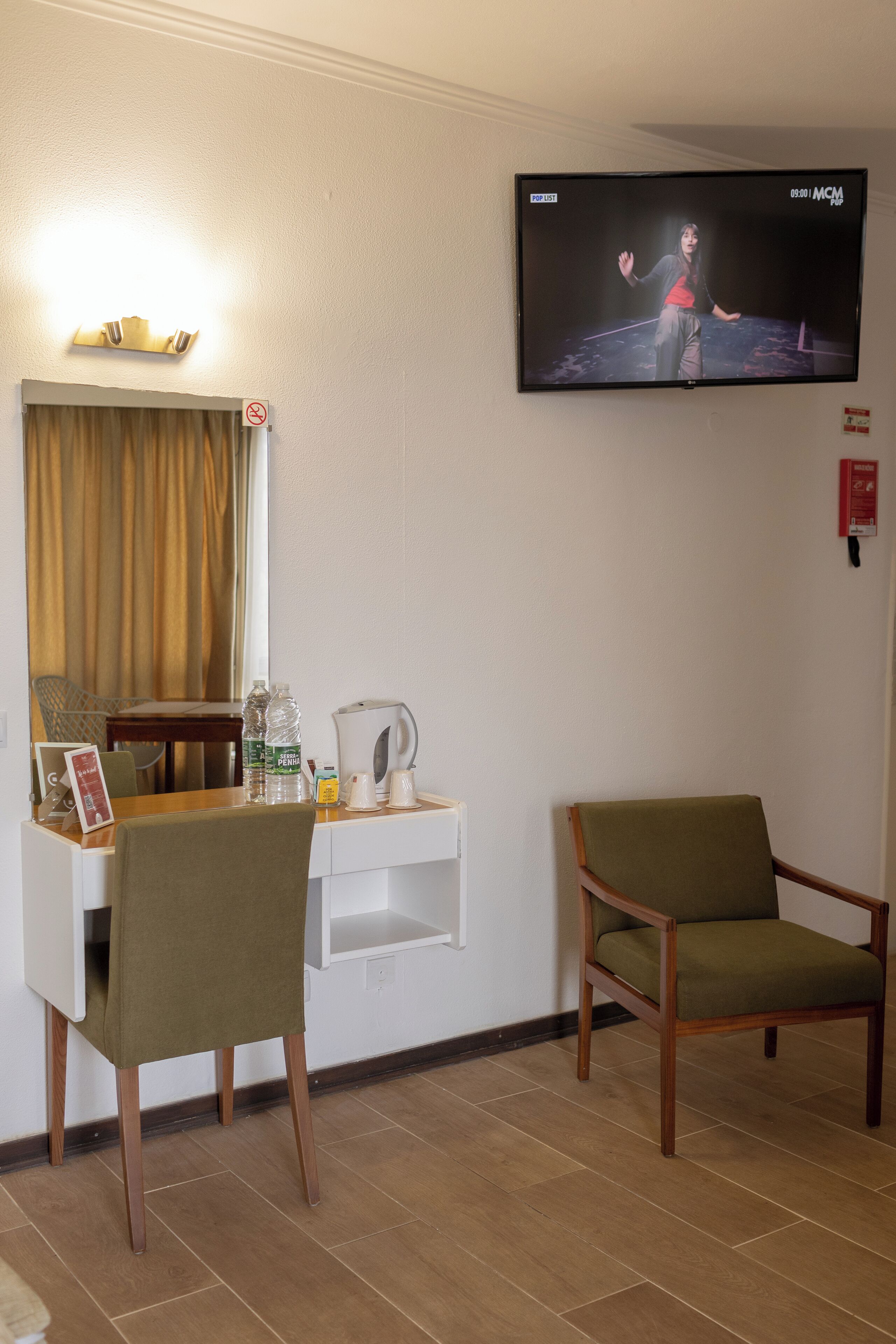 Habitación de hotel con escritorio, dos sillas, televisor, espejo y ventana con cortinas.