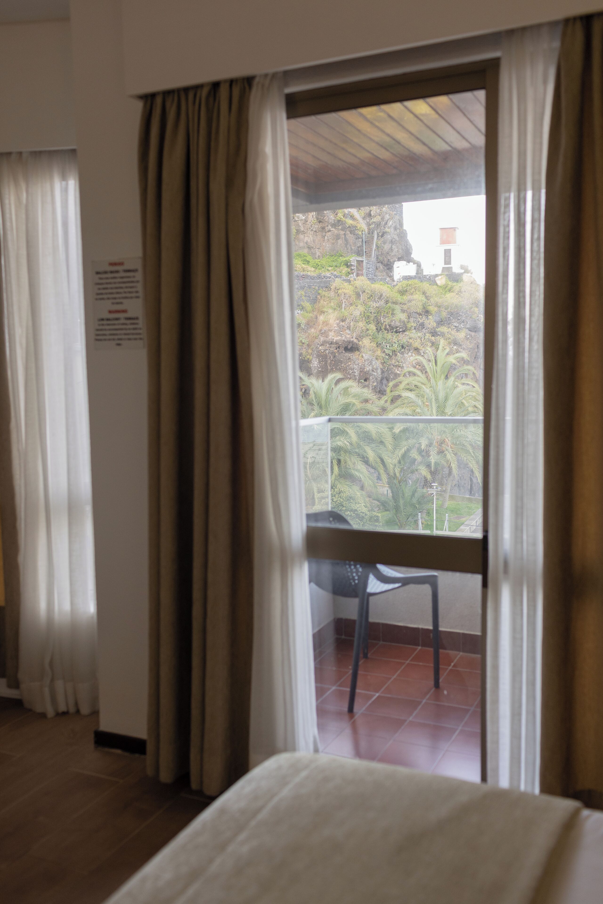 A room with a balcony, a chair, and curtains.