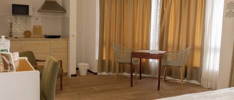 A hotel room with a dining table, two chairs, a bed, a kitchen area with a microwave, and a window with curtains.