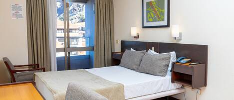 Habitación de hotel con cama, escritorio, silla, mesita de noche con teléfono y ventana con cortinas.