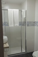 A modern bathroom with a glass shower enclosure, white tiles, and a visible toilet.
