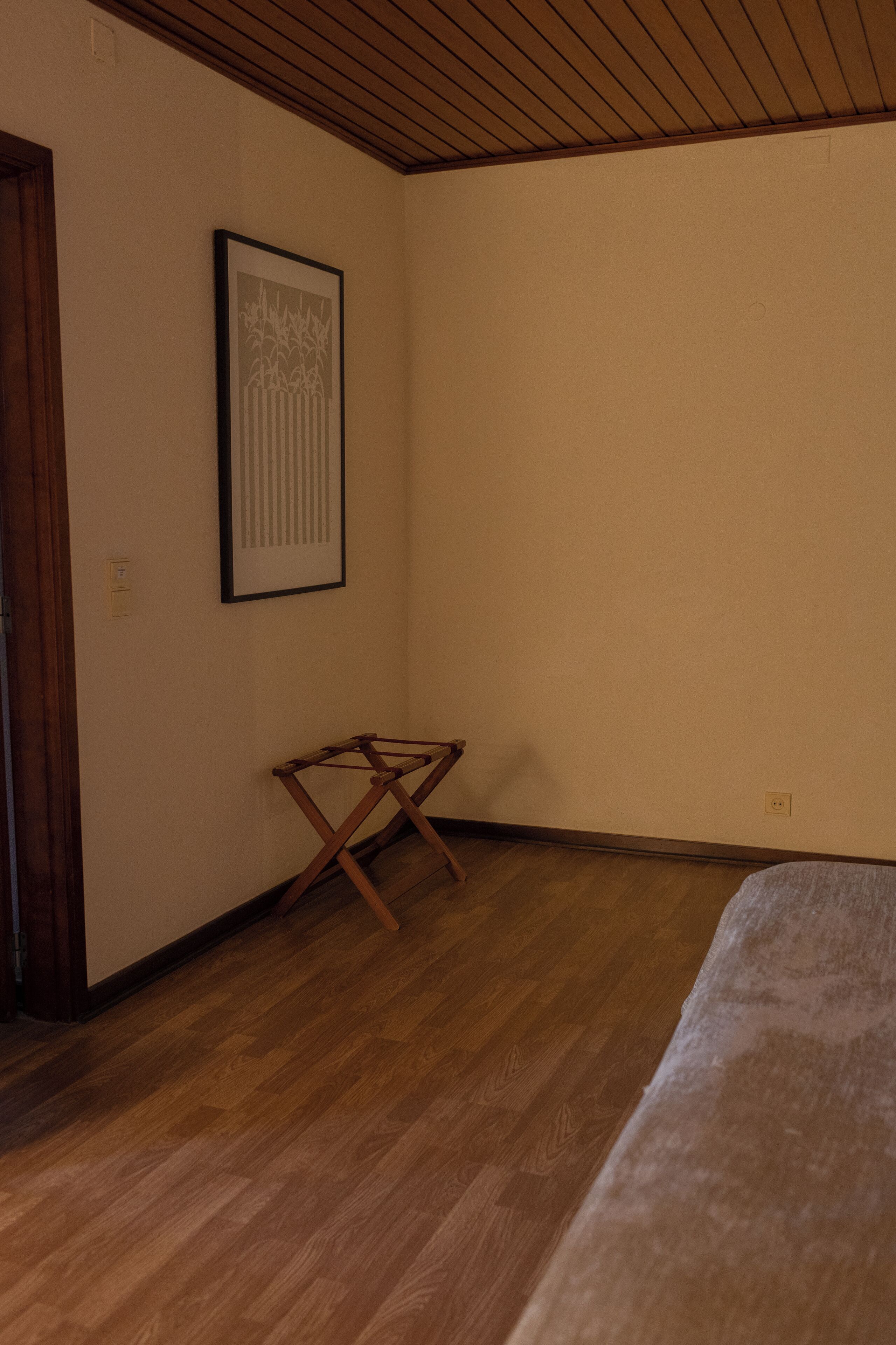 A room with wooden flooring, a framed picture on the wall, and a wooden folding chair.