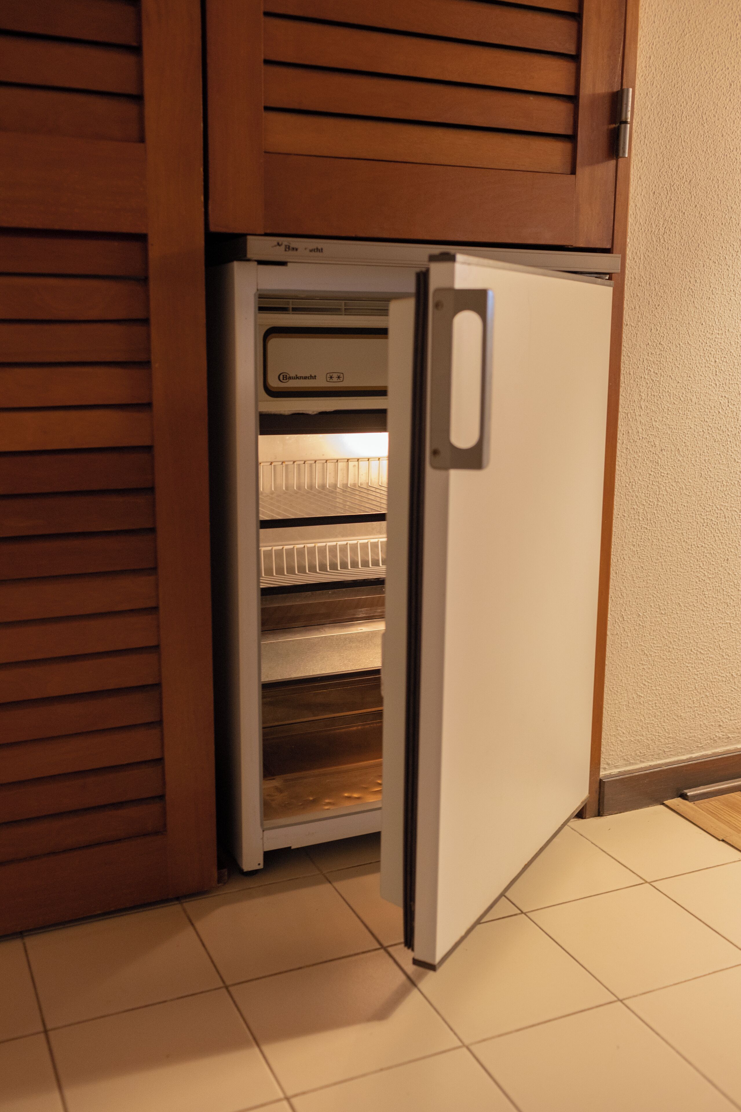 Un petit réfrigérateur doté d’un compartiment congélateur, installé dans une cuisine avec des meubles en bois et un sol carrelé.