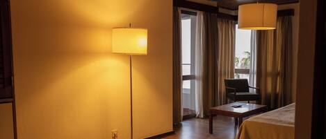 Et hotelværelse med trægulv, seng, skrivebord, stol og lampe.