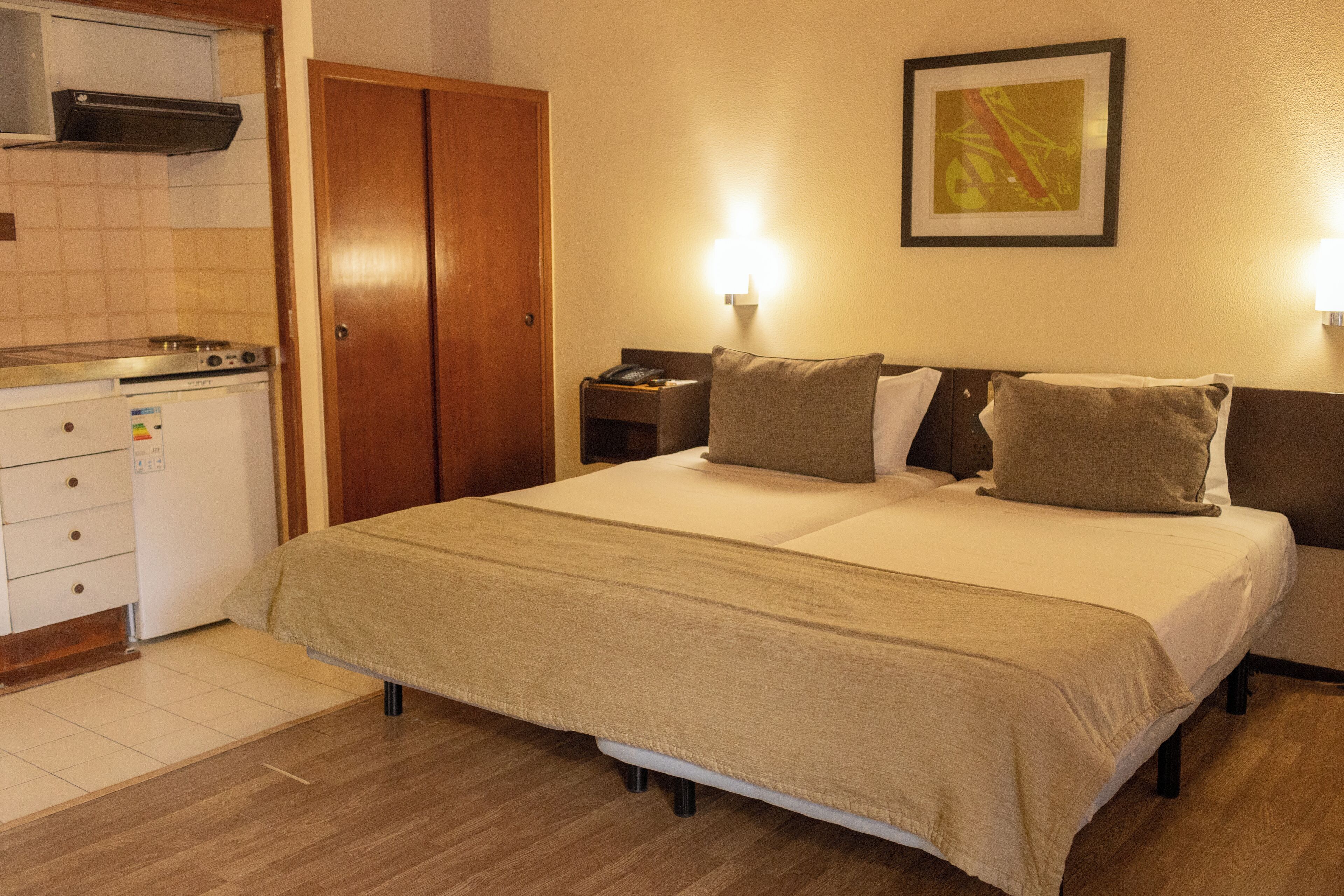 A hotel room with a bed, bedside tables, a small kitchenette, and a wardrobe.