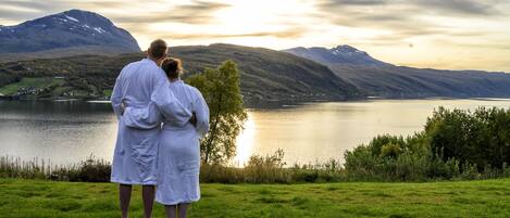 A couple standing on a wooden deck overlooking a lake with mountains in the background.