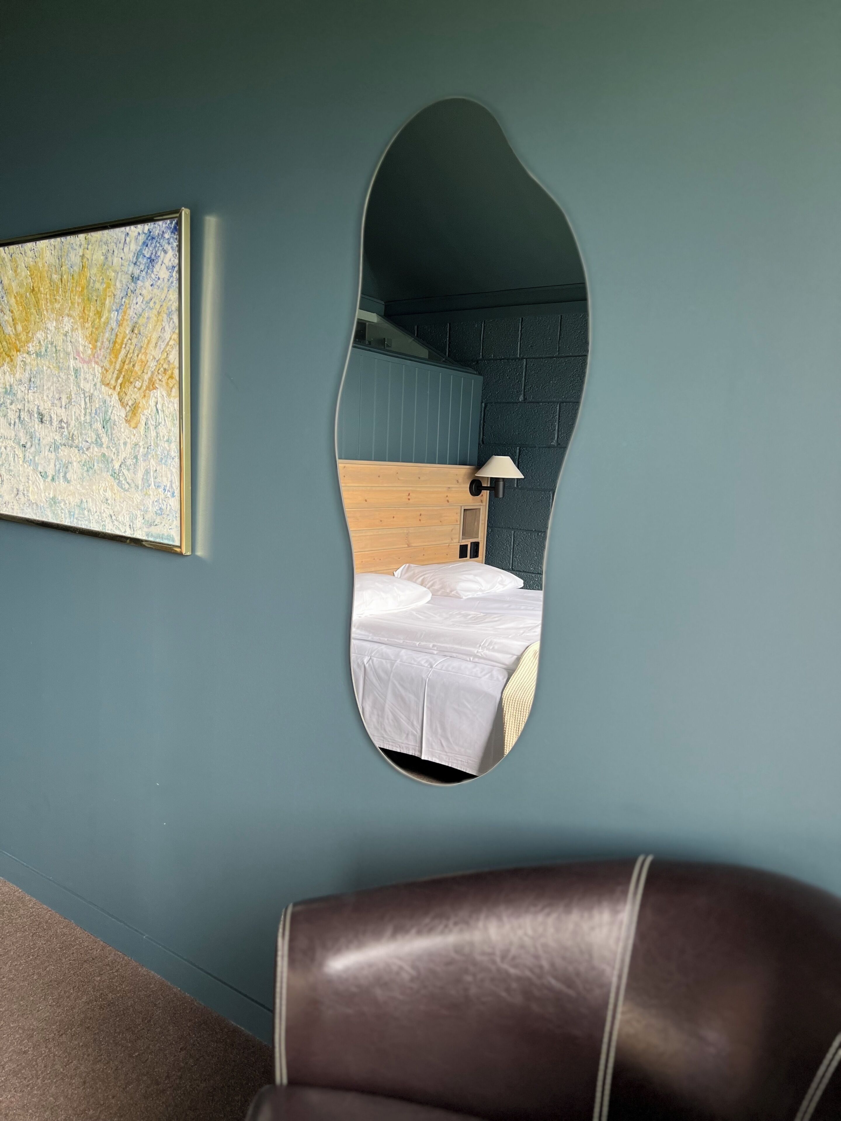 A bedroom with a bed, a wooden headboard, a nightstand, a lamp, and a painting on the wall.