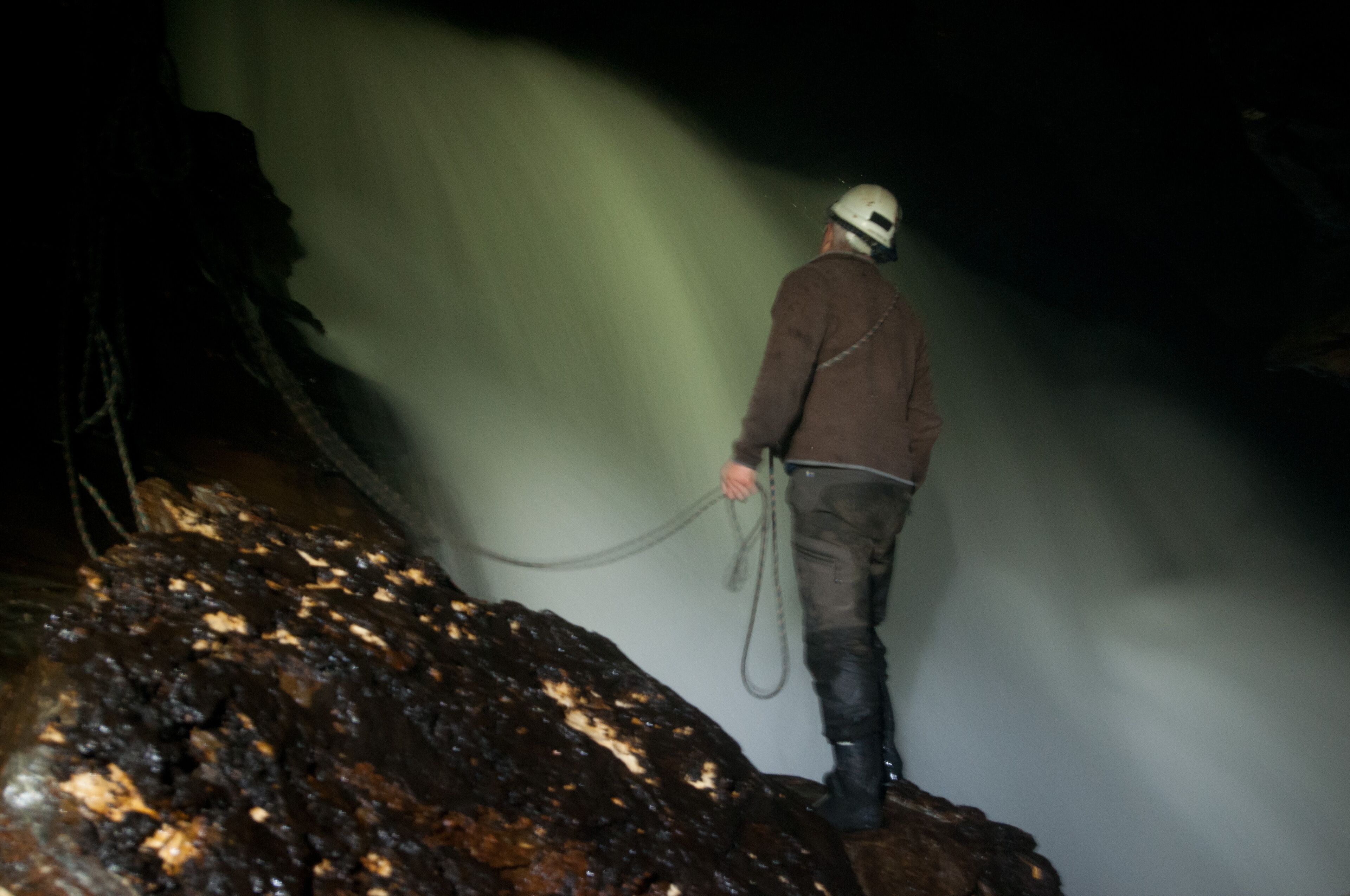 Una persona sobre una roca sosteniendo una cuerda, con una cascada al fondo.