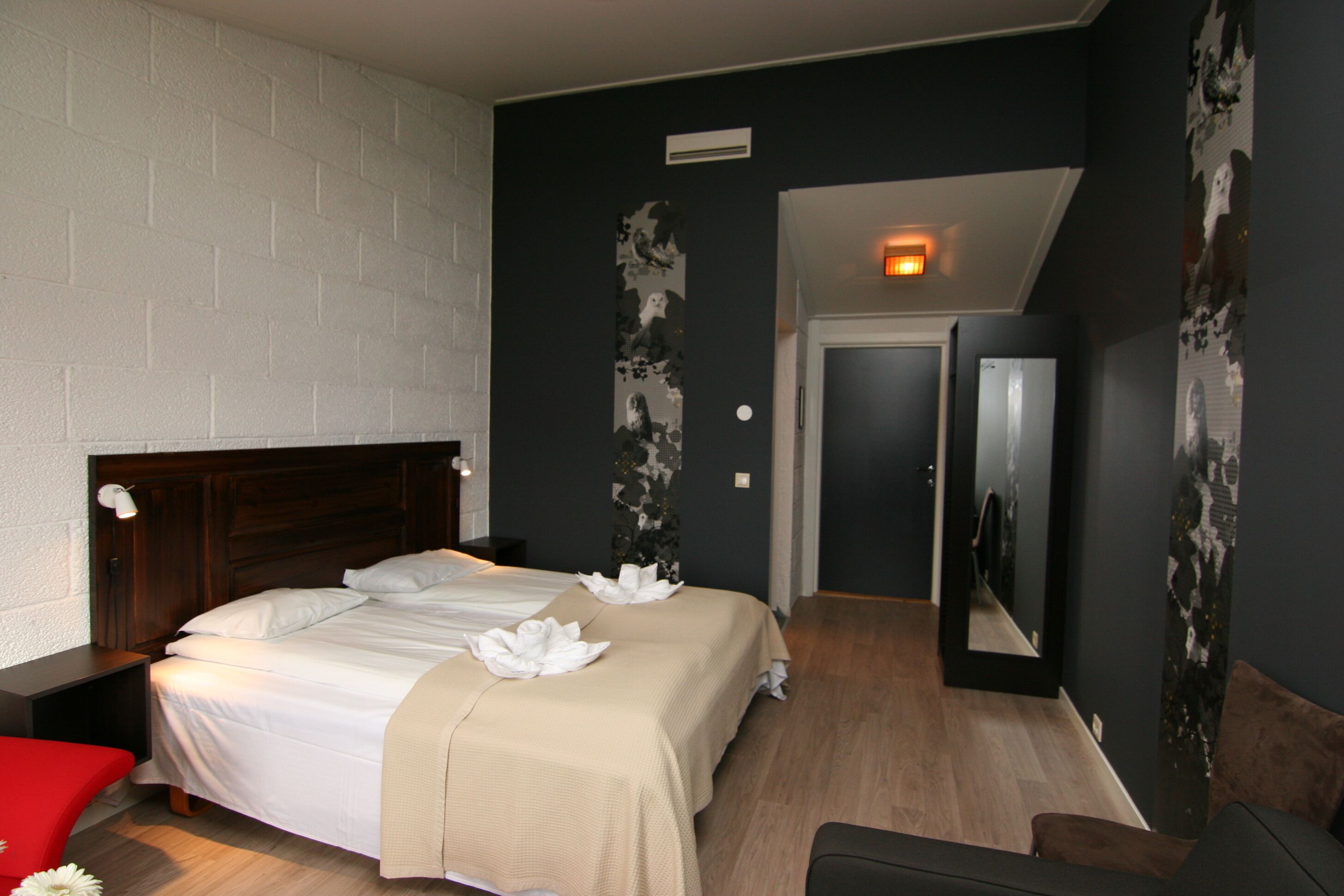 A bedroom with a large bed, a wooden headboard, a red chair, and a mirror on the wall.