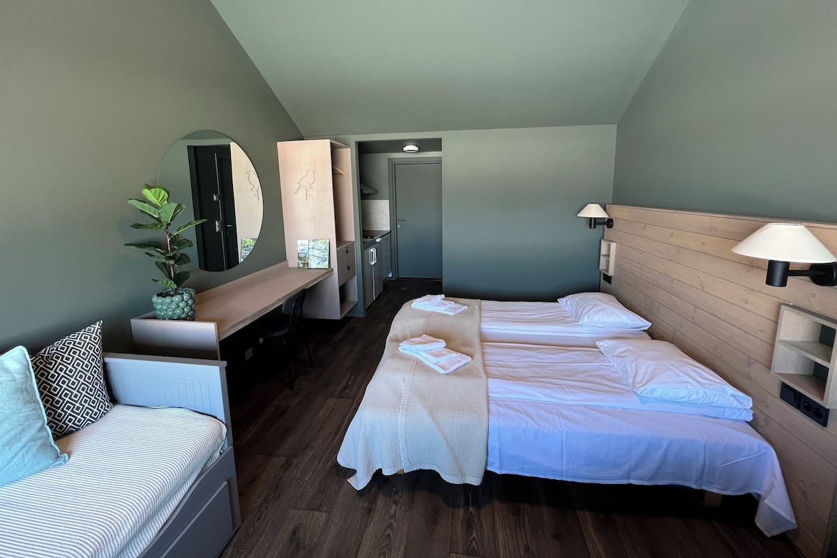 Quarto de hotel com cama, escrivaninha, cadeira, espelho e planta.