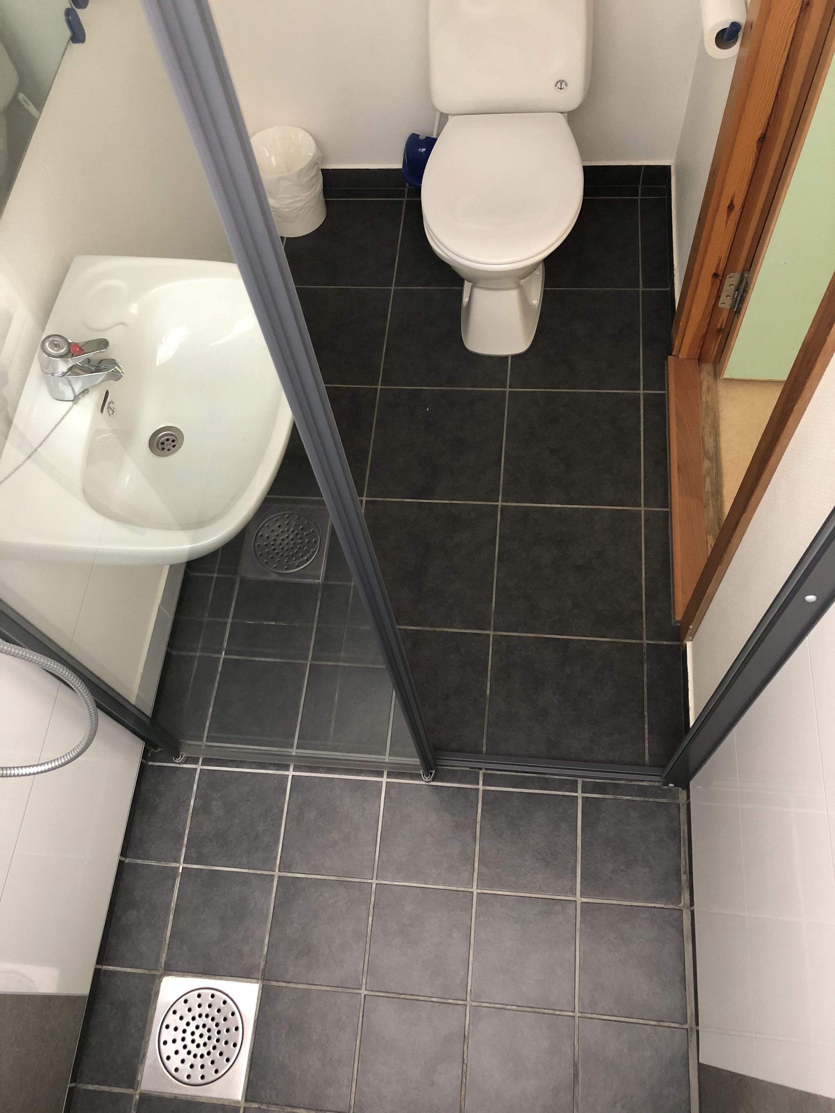 Et badeværelse med en hvid vask, toilet og mørkt flisegulv.