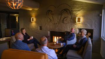 A group of people seated around a table in a warmly lit room with a fireplace, stone walls, and a unique wall art of a ram's head.