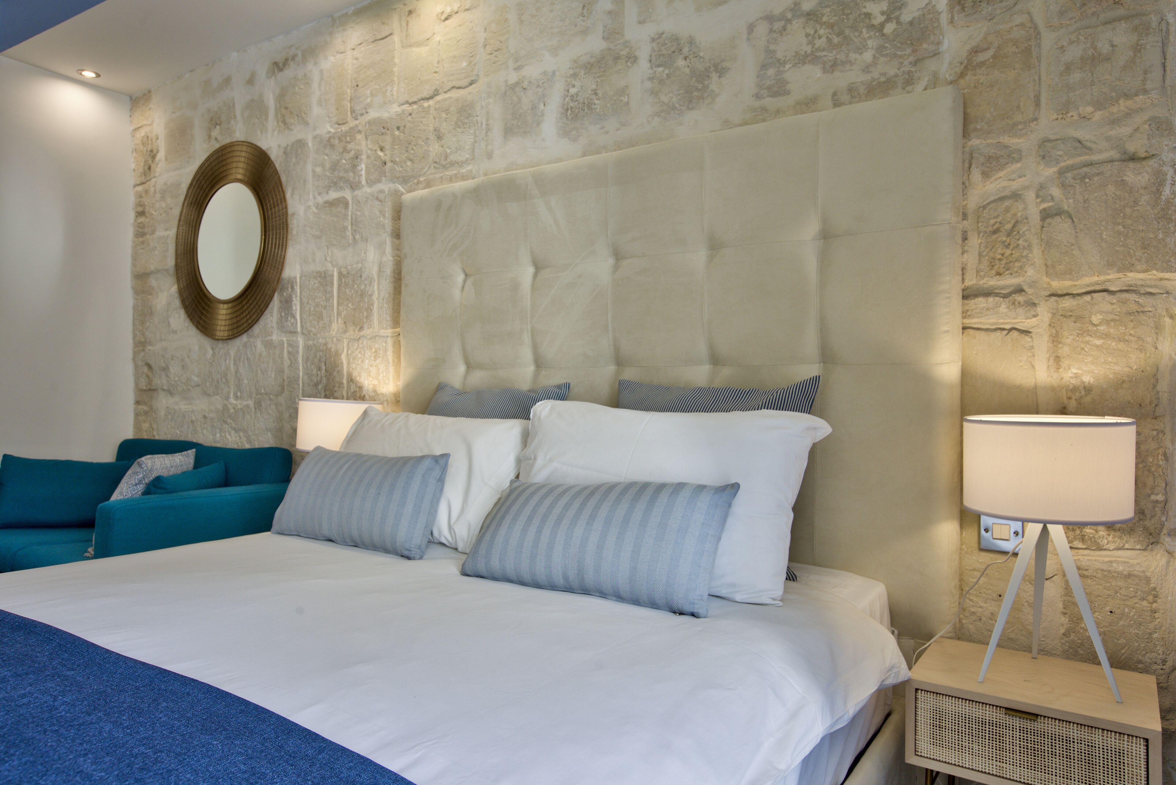 A bedroom with a large bed, a stone wall, a round mirror, and a bedside lamp.