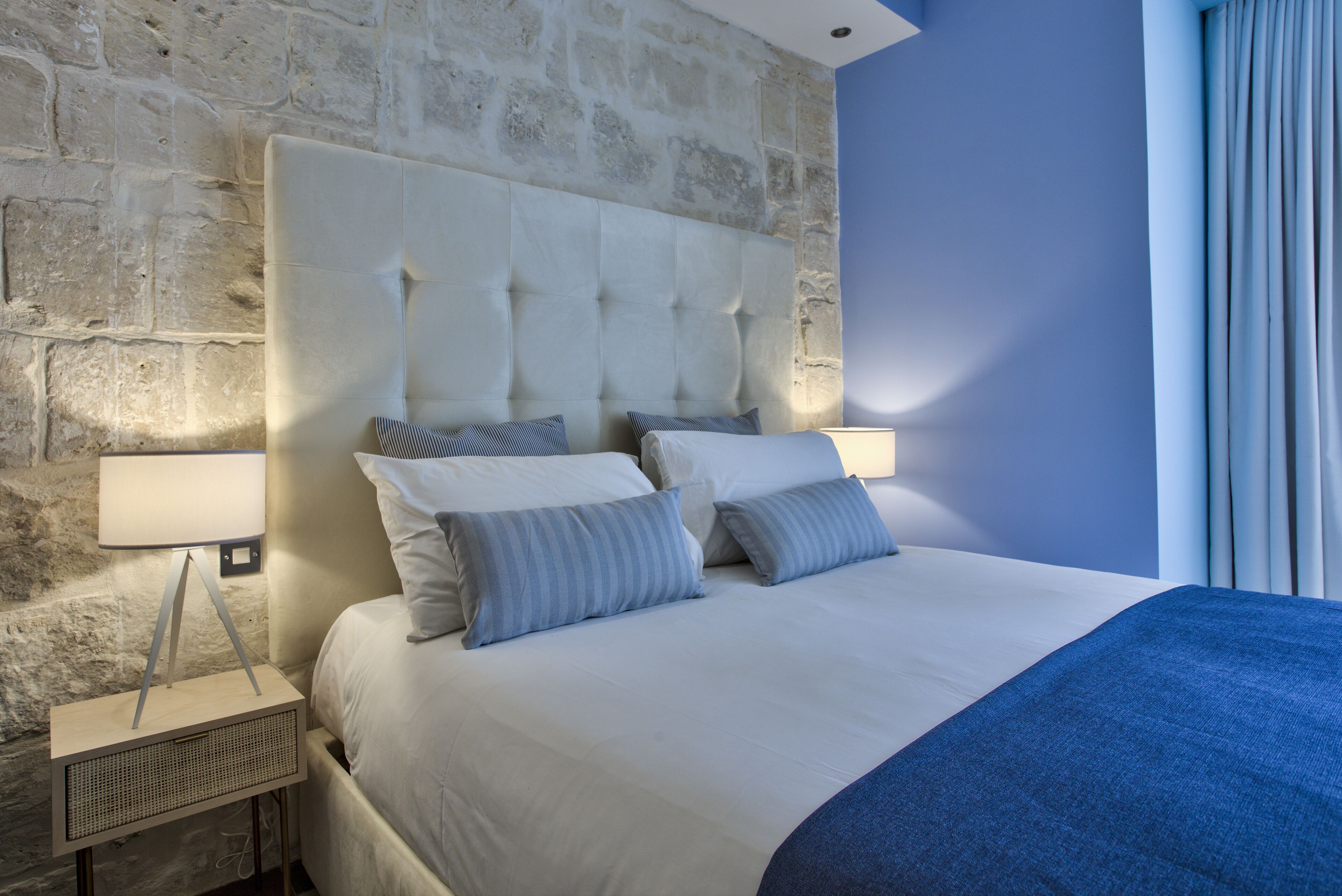 A neatly made bed with a tufted headboard, a bedside lamp, and a blue throw blanket.